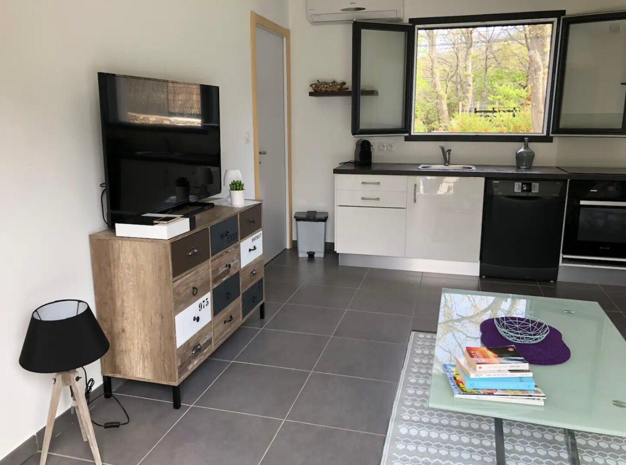 A modern kitchen with a built-in oven, a dishwasher, and a window with a view of trees.