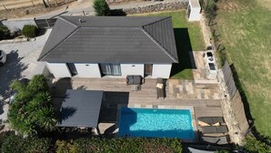 A two-story house with a swimming pool, patio furniture, and a stone wall.