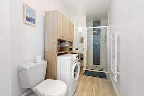 Ein kleines Badezimmer mit Toilette, Waschmaschine und Duschbereich.