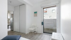 Une chambre à coucher comprenant un lit, une chaise, un radiateur et une porte-fenêtre coulissante donnant sur un balcon.