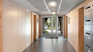 Un couloir aux murs recouverts de lambris en bois, une entrée avec une porte en verre et un espace équipé de casiers métalliques.