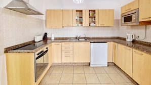 A modern kitchen with wooden cabinets, a stainless steel range hood, a built-in microwave, and a dishwasher.