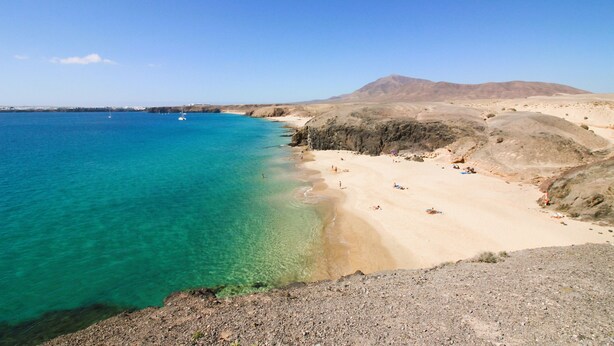 A coastal beach with clear turquoise waters, sandy shore, and rocky terrain.