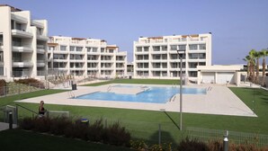 Ein modernes Gebäude mit mehreren Balkonen, einem zentral gelegenen Pool und einem gepflegten Rasen.