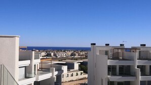 Ein modernes Gebäude mit mehreren Balkonen, freiem Blick auf das Meer und einer entfernten Stadtlandschaft.