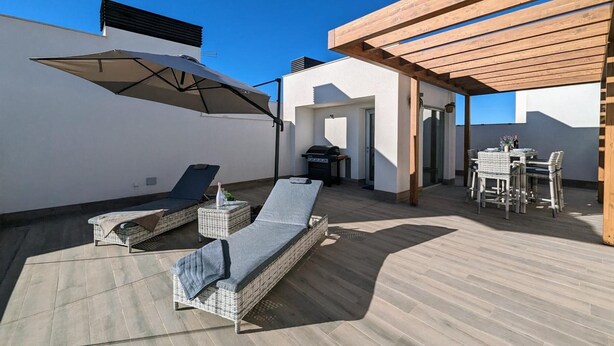 Eine Dachterrasse mit Liegestühlen, einem Tisch und einem Grill.