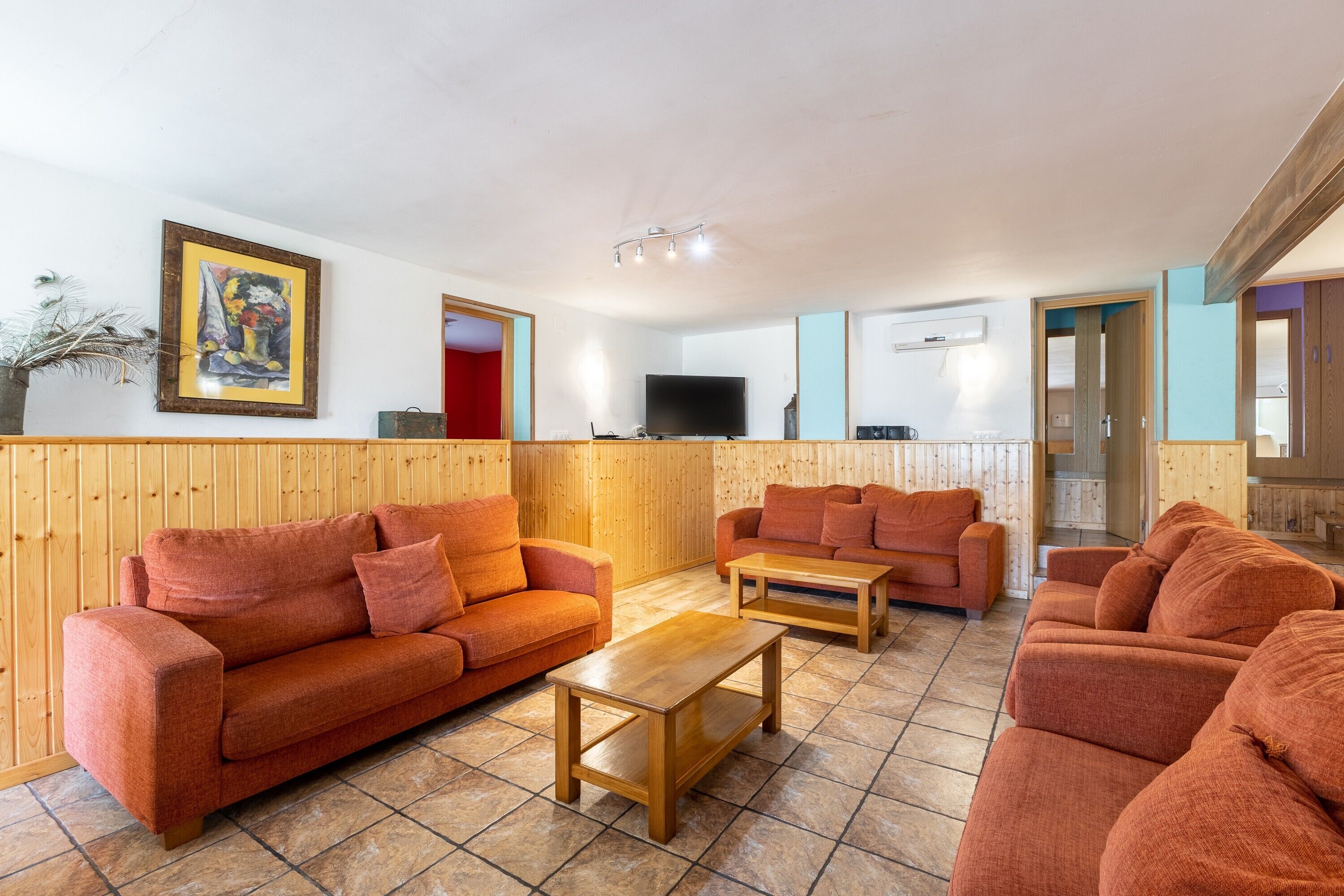 A room with wooden paneling, two sofas, a coffee table, a flat-screen TV, and a painting on the wall.