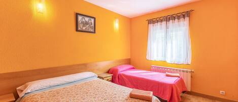 Habitación con dos camas, cabecera de madera, ventana con cortinas traslúcidas y radiador.