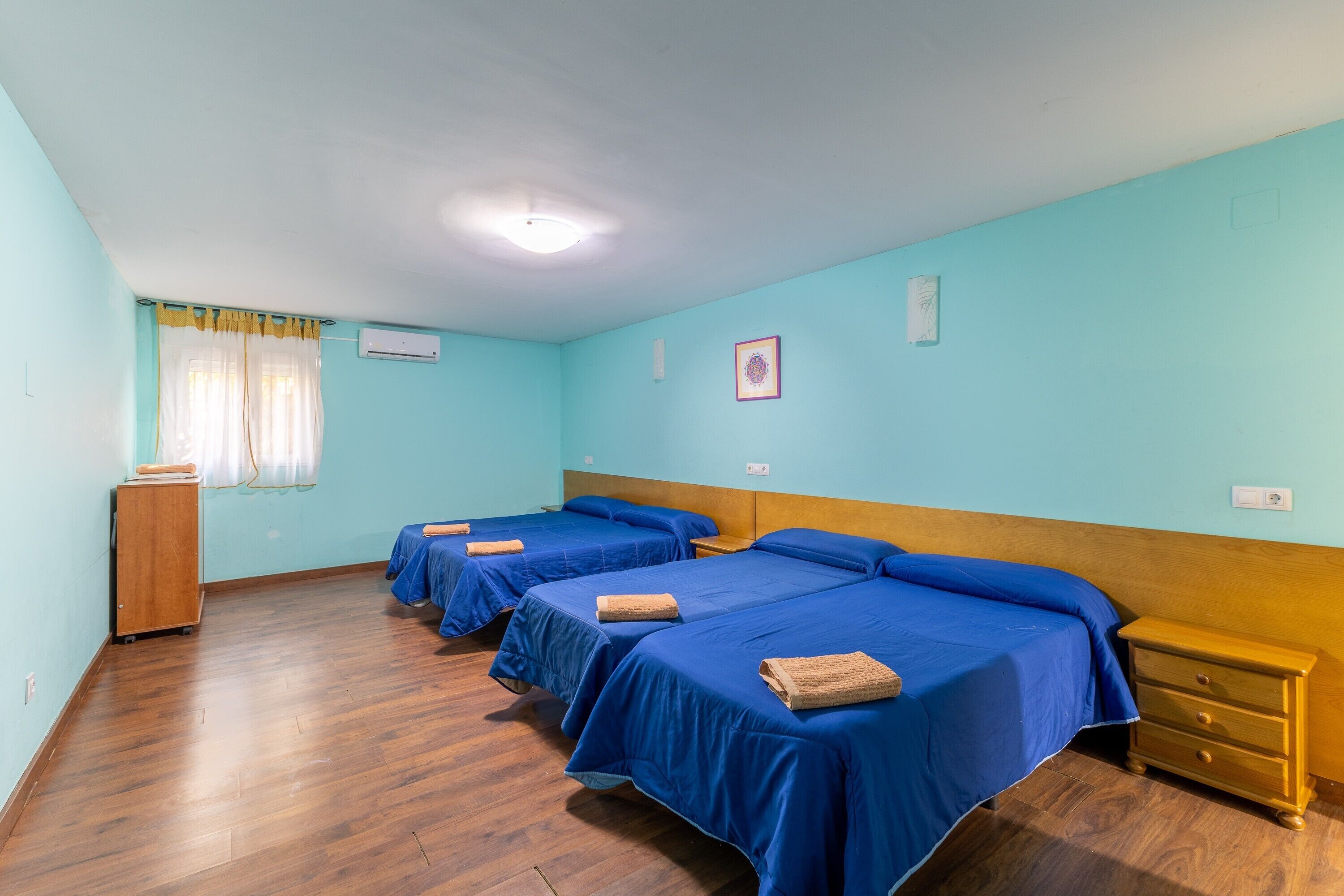 A room with three beds, wooden floors, a wooden dresser, and a window with curtains.