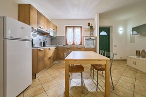 A kitchen with a refrigerator, oven, microwave, wooden cabinets, a dining table with chairs, and a window with curtains. - Apartment 'Casa Martina' with Mountain View, Private Terrace and Wi-Fi (Sassetta)