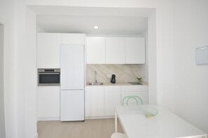 Eine moderne Küche mit weißen Schränken, einem eingebauten Backofen, einem Kühlschrank, einer Spüle und einer Marmor-Spritzschutzwand.