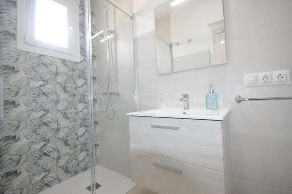 Un baño con ducha, lavamanos, espejo y retrete.