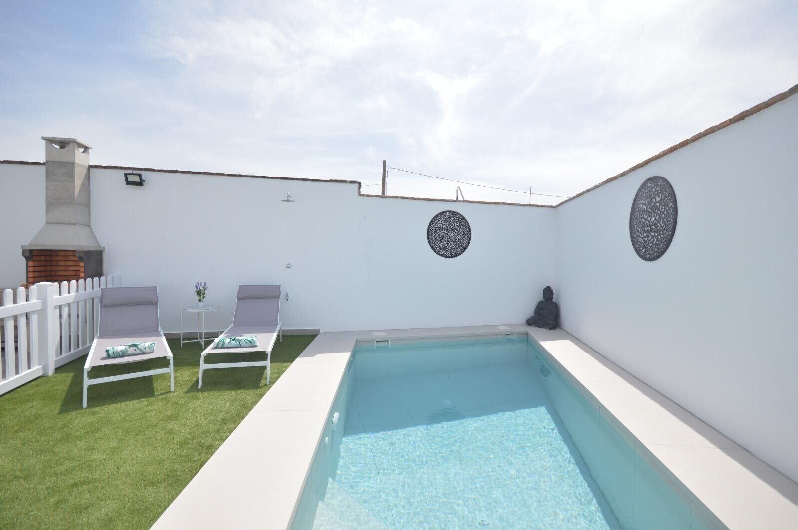 Ein Poolbereich mit weißer Wand, zwei Liegestühlen, einem kleinen Tisch und einer Statue.
