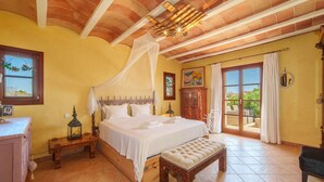 A spacious bedroom with a large bed, a wooden bench, a nightstand, and a view of the outdoors through a sliding glass door.