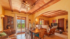 A spacious living area with a wooden dining table, comfortable seating, and a view through a glass door to the outdoors.