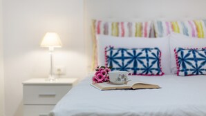 A neatly made bed with a patterned pillow, a cup, and a book on a bedside table.