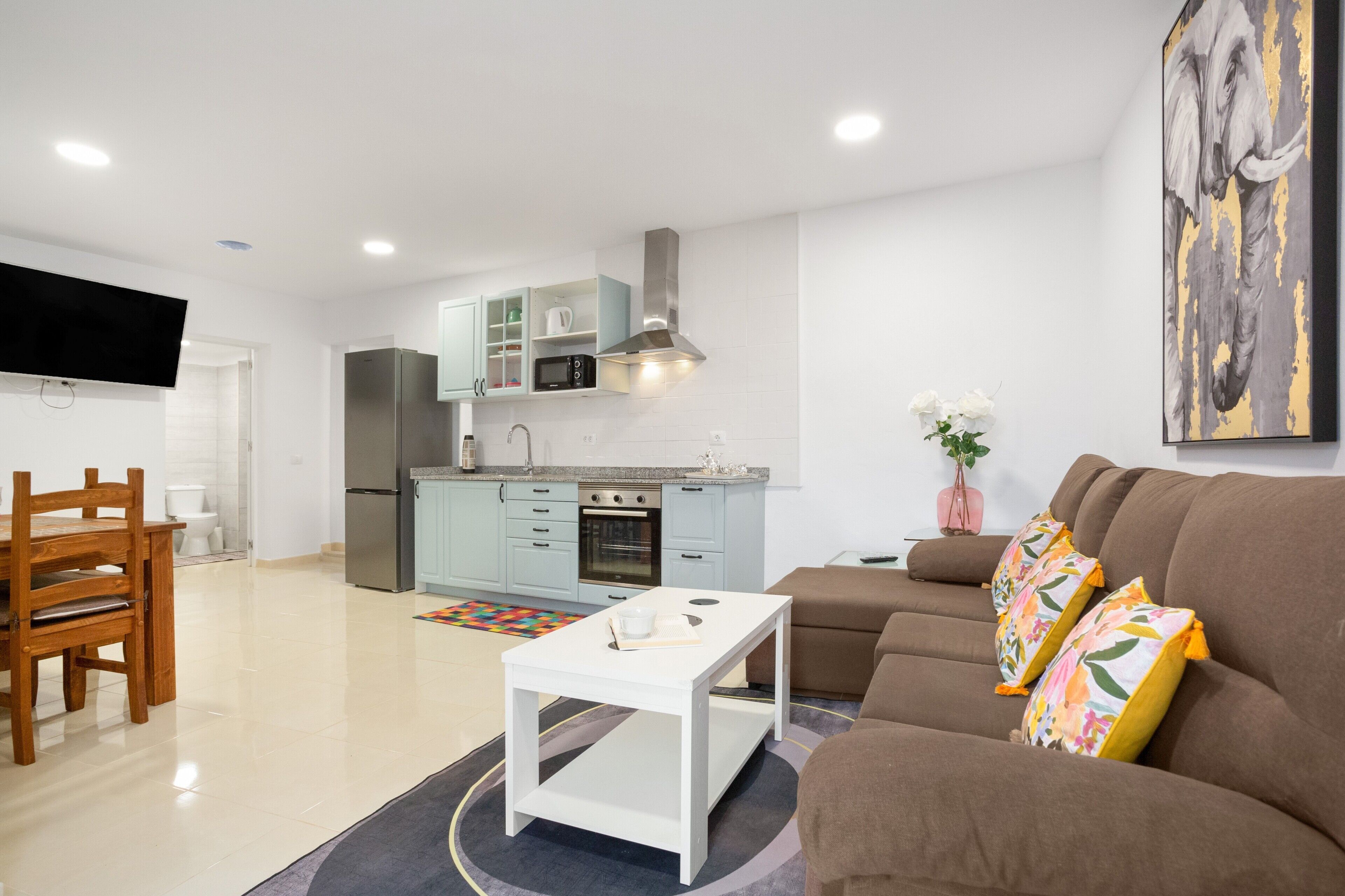 A modern living room with a sofa, a coffee table, and a kitchen area with cabinets and appliances.