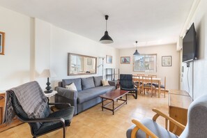 A living room with a sofa, chairs, a coffee table, a dining table with chairs, a TV, and framed pictures on the walls. - Apartment 'Zambra 3 - 311' with Shared Pool, Wi-Fi and Air Conditioning (La Manga del Mar Menor)