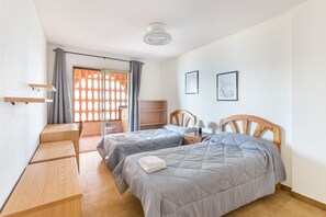 Ein Schlafzimmer mit zwei Betten, einem Schreibtisch, einem Stuhl, einem Deckenventilator und einem Fenster mit Vorhängen.