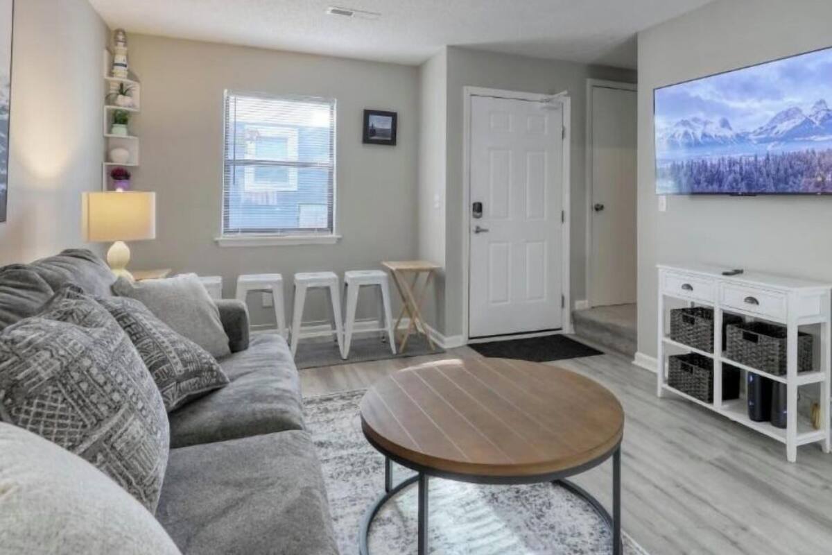 A living room with a grey sofa, a round coffee table, a TV, and a white cabinet with baskets.