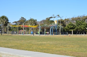 An outdoor park with playground equipment, a covered seating area, and trees in the background. - Small Peace of Paradise,  In beautiful Oak Island (Oak Island)