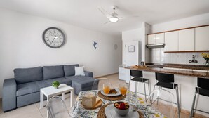 Une cuisine moderne avec des meubles blancs, un coin repas avec une table mise pour le petit-déjeuner et un canapé gris dans le salon.