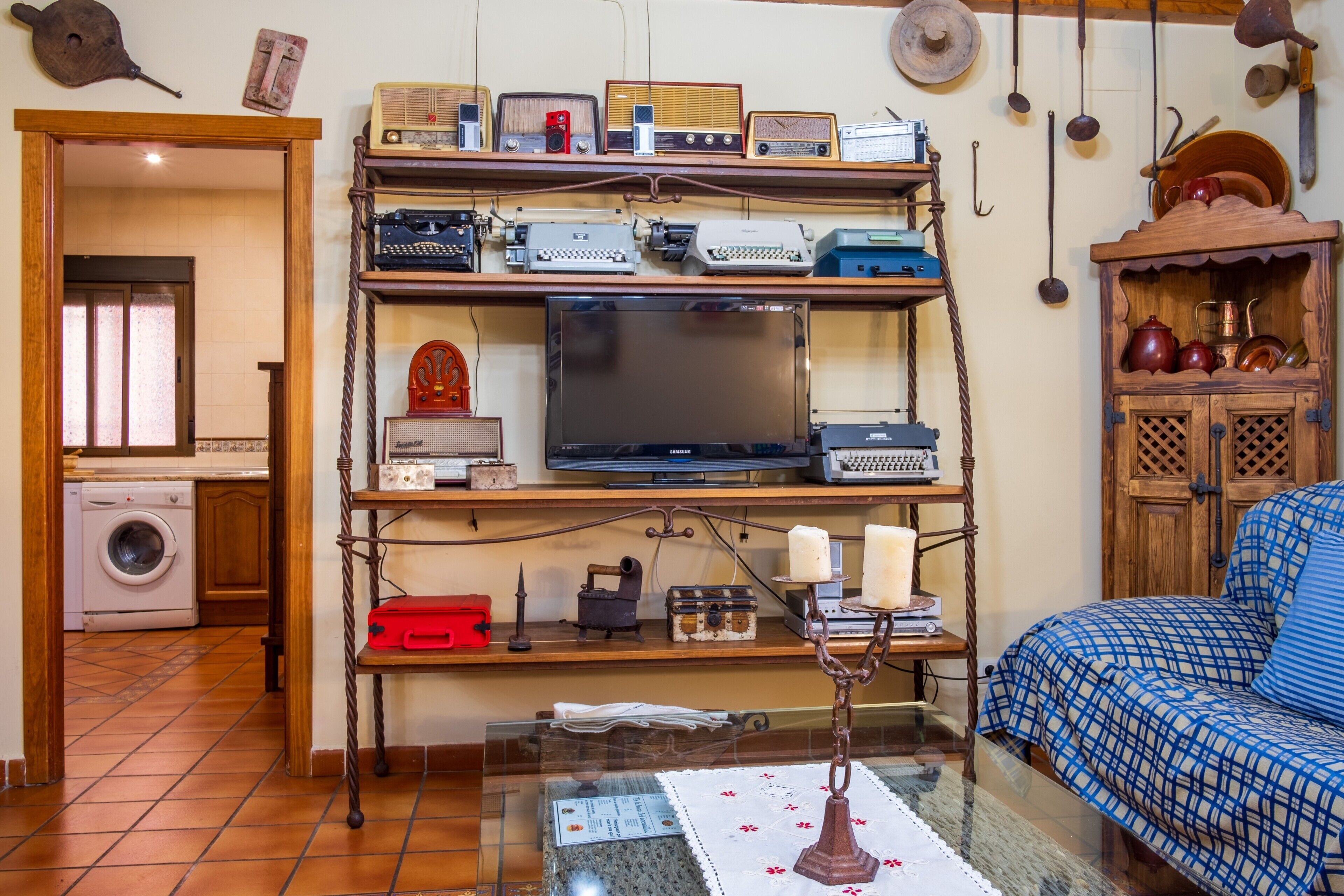 Una sala de estar con una mesa de centro de vidrio, un sofá, un televisor y una estantería con diversos objetos.