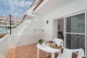 A balcony with a table set for two, a small plant, a pitcher, and a plate of food.