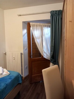 A bedroom with a bed, a wooden door, a radiator, and a chair.