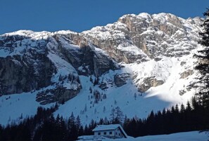 A mountain with snow-covered peaks and a small building at its base.