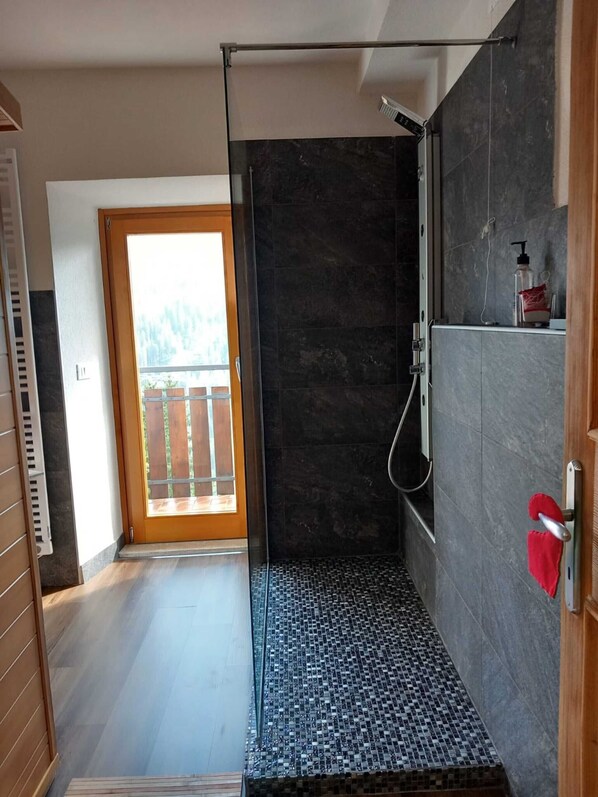 Une salle de bain moderne avec une douche, une porte vitrée donnant sur un balcon et un sol carrelé.