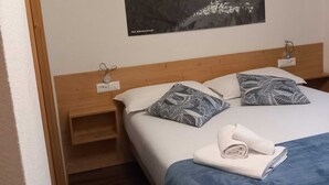 Et soveværelse med en seng, puder, et natbord, et billed monteret på væggen og en trægavl.
