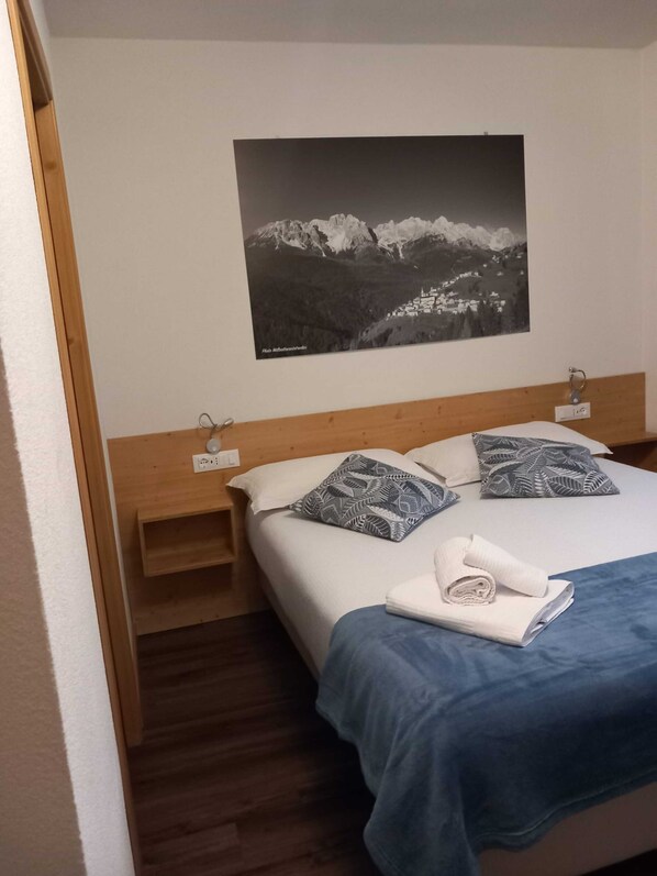 Ein Schlafzimmer mit Bett, Kissen, einem Nachttisch, einem Wandbild und einem Holzkopfstück.