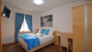 A bedroom with a bed, a desk, a chair, a television, and a window with curtains.