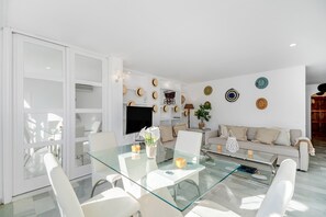 Un salon moderne avec une table basse en verre, des canapés blancs et un téléviseur.