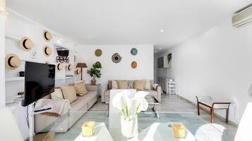 A modern living room with a flat-screen TV, a glass coffee table, and a sofa.