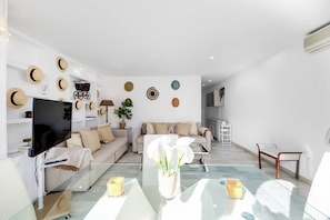A modern living room with a flat-screen TV, a glass coffee table, and a sofa.