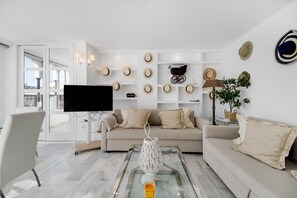 A modern living room with a sofa, a flat-screen TV, a glass coffee table, and a wall decorated with hats. - Apartment 'Vistahermosa' with Shared Pool, Wi-Fi and Air Conditioning (El Puerto de Santa María)