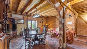 Un interior rústico con vigas de madera a la vista, pared de ladrillo, una mesa redonda de madera y una zona de estar acogedora.