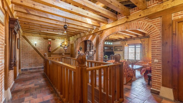Interior de madera con una escalera, paredes de ladrillo y barandilla de madera.