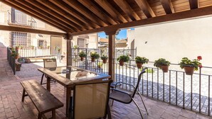 Un patio al aire libre cubierto con vigas de madera, una mesa, sillas y plantas en macetas.