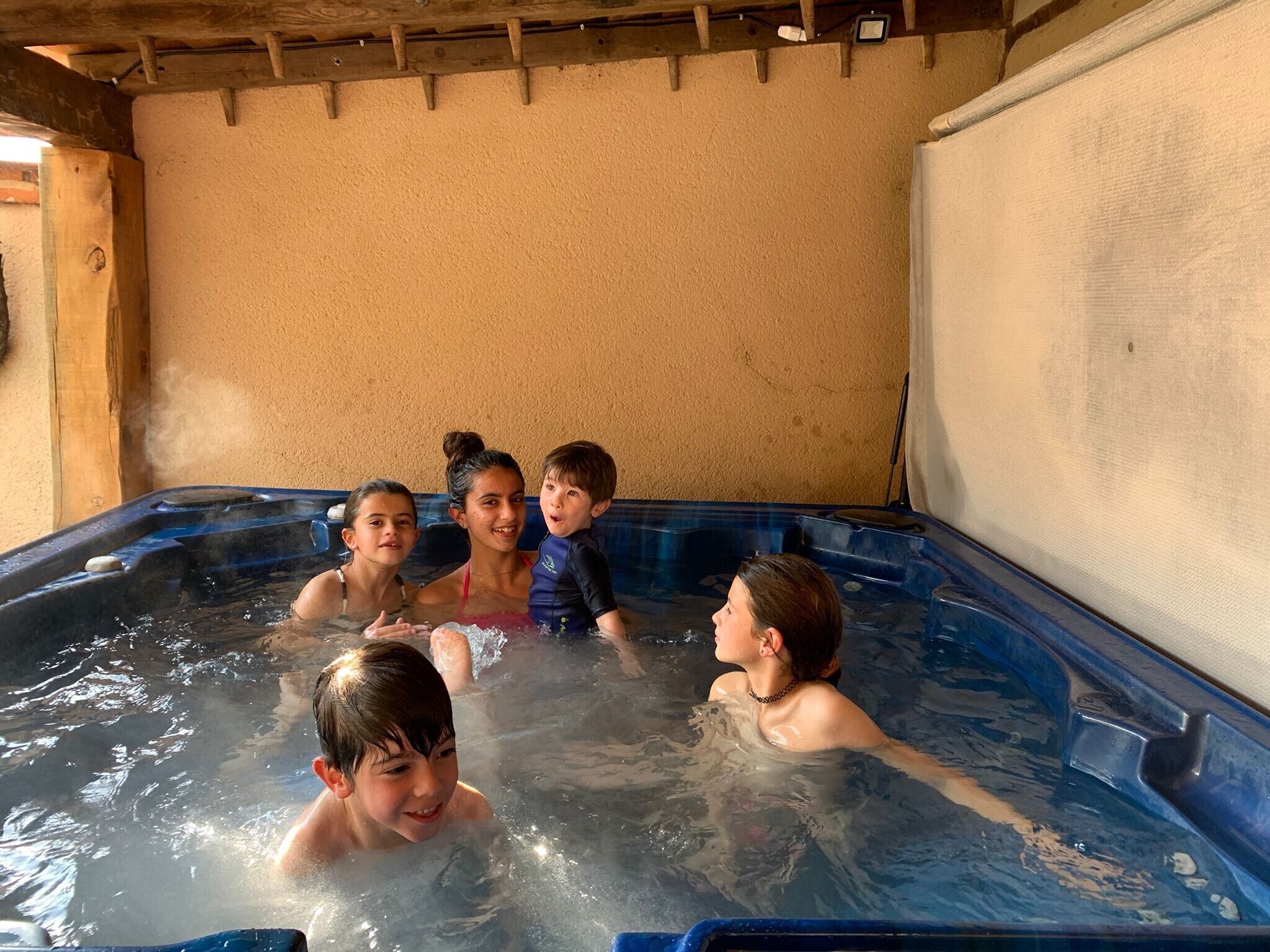 A group of children in a hot tub with a wooden ceiling and beige walls.