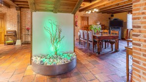 Un interior rústico con vigas de madera a la vista, pared de ladrillo, zona de comedor con mobiliario de madera y una escultura iluminada única.
