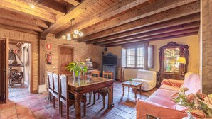 Un interior rústico con vigas de madera a la vista, pared de ladrillo, mesa de comedor con sillas, sofá y chimenea.