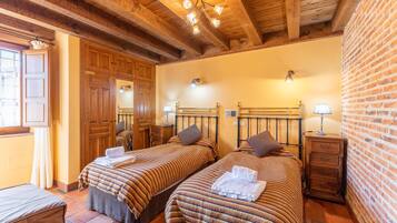 Una habitación con dos camas, vigas de madera, paredes de ladrillo y un pequeño armario de madera.