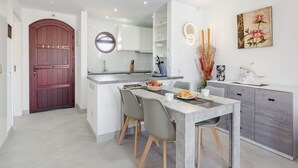 A modern kitchen with a dining area, featuring a marble countertop, a built-in oven, and a round mirror above the sink.