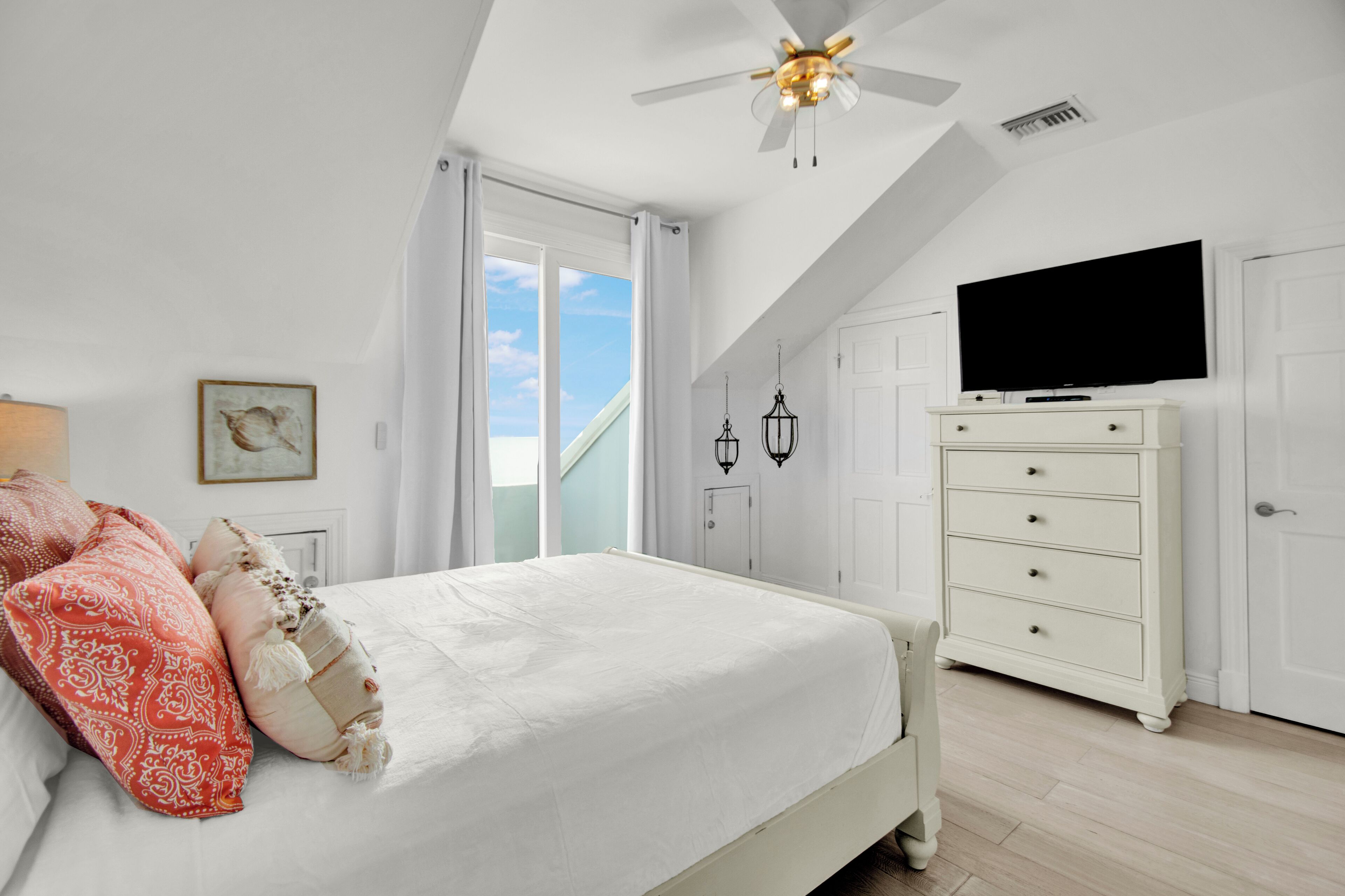 A bedroom with a bed, a dresser, a television, and a ceiling fan.