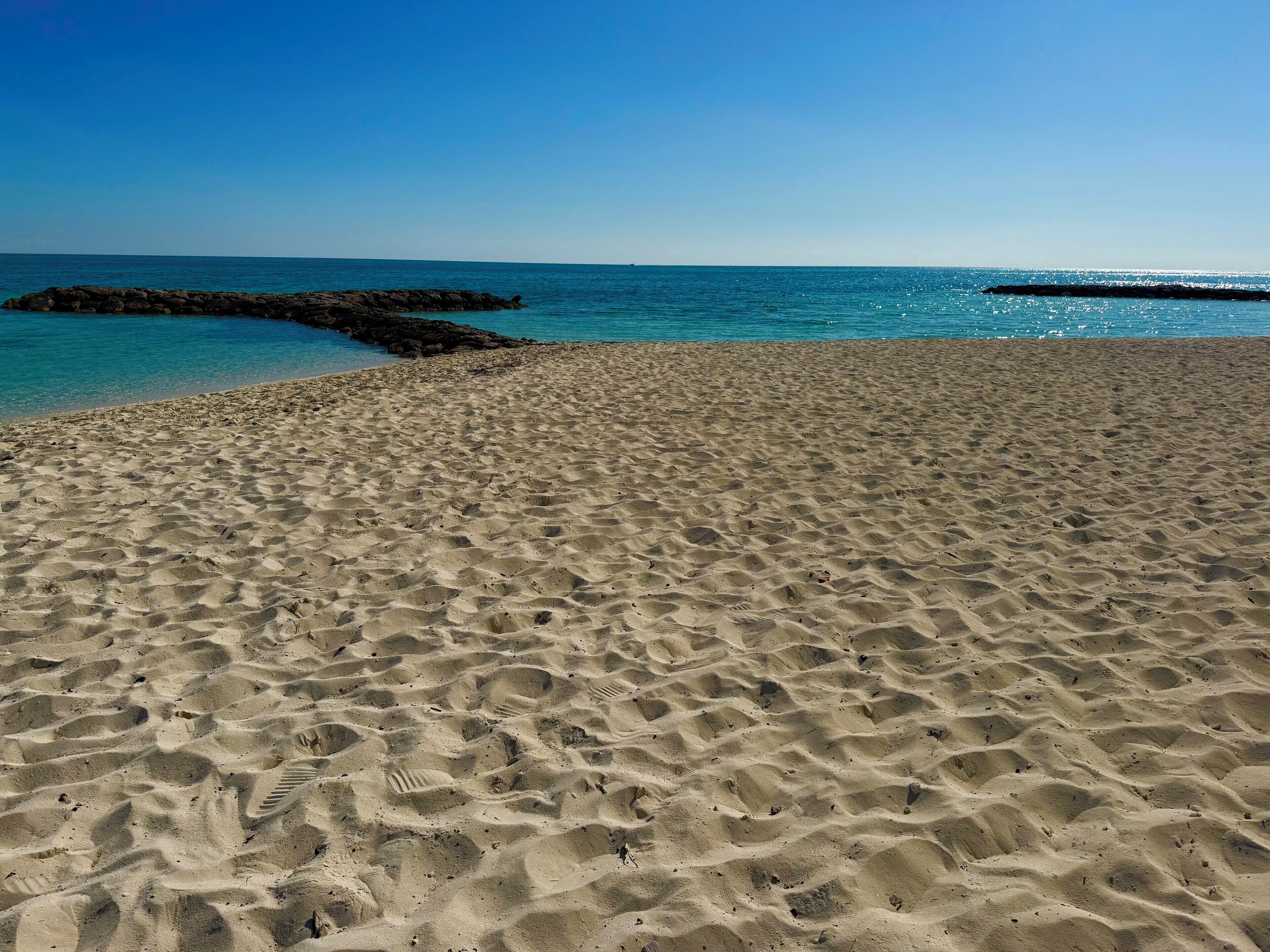 Une plage de sable avec des empreintes et un affleurement rocheux dans l’eau.