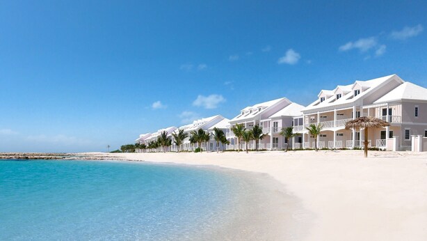 Een hotel aan het strand met witte gebouwen, palmbomen en helderblauw water.