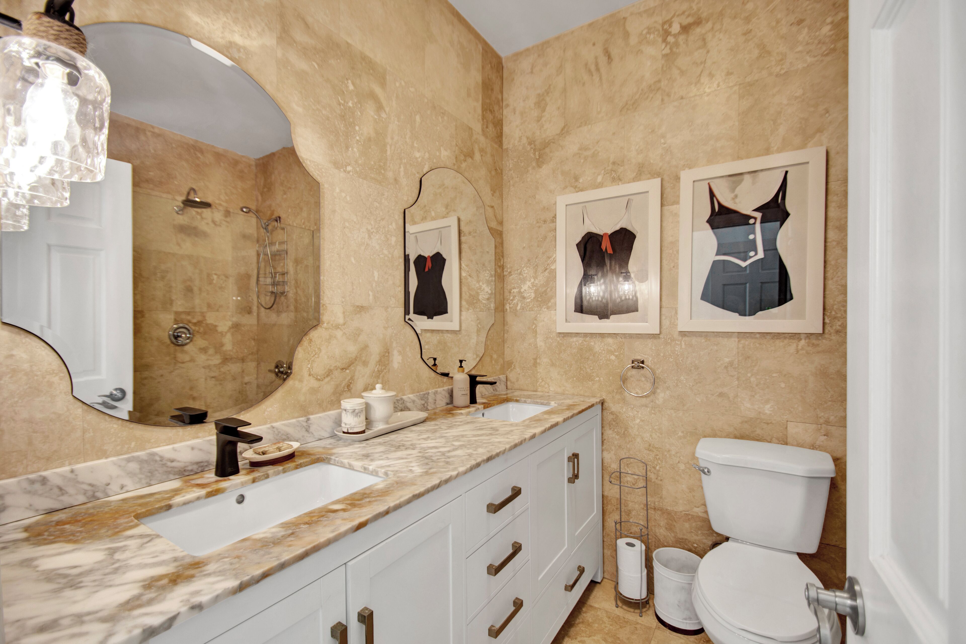 A bathroom with marble countertops, a large mirror, a white toilet, and two framed artwork pieces on the wall.